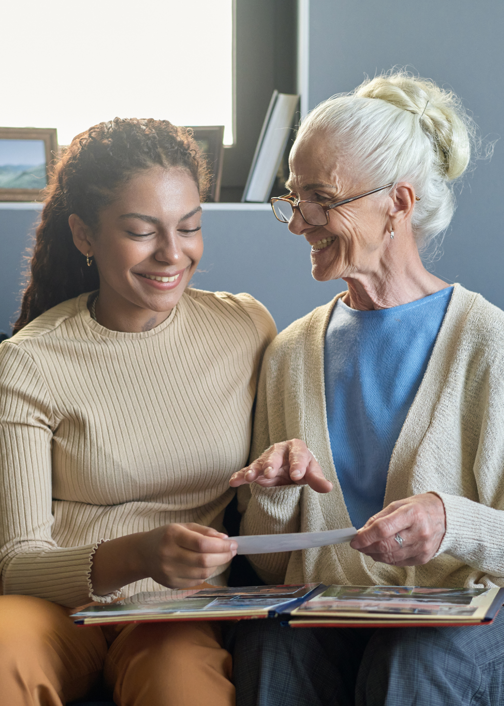 Smiling elderly woman with caregiver reviewing photo album