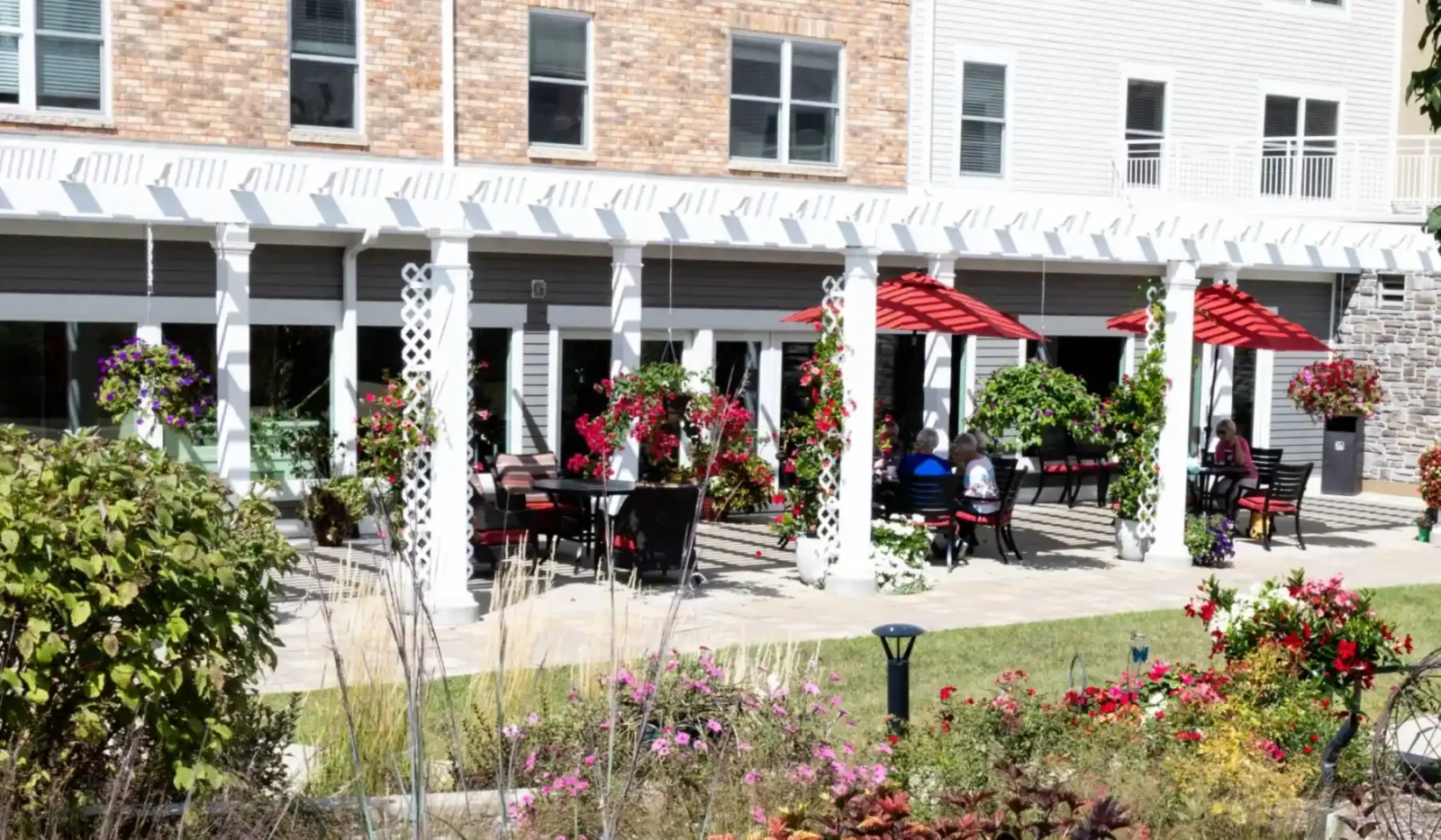 Exterior view of Cottage Grove Place senior living community patio with tables and umbrellas and with landscaped grounds