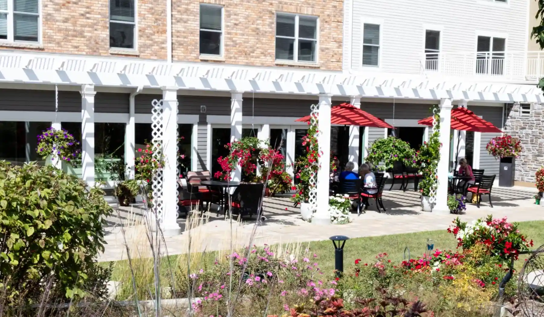 Exterior view of Cottage Grove Place senior living community patio with tables and umbrellas and with landscaped grounds