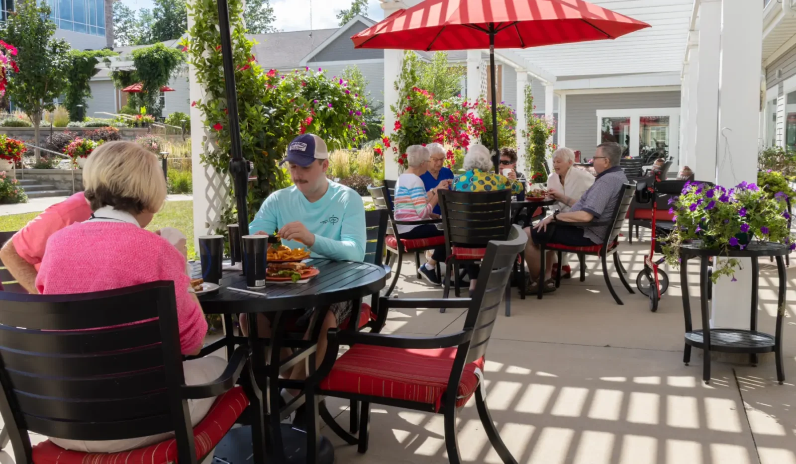 Exterior view of Cottage Grove Place senior living community patio with tables and umbrellas and with landscaped grounds